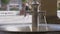 Close-up hot springs water flowing from metal faucet with blurred unrecognizable people passing on city street at