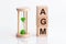 Close-up of an hourglass next to wooden blocks with the text AGM. AGM - Annual general meeting