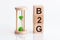 Close-up of an hourglass next to wooden blocks with the text B2G. B2G - Business-to-government