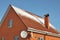 A close-up of a house from red brick with two satellite dish antennas, rain gutter system, a chimney, and a gable steep metal