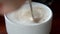 Close up of human hand using teaspoon stirring hot coffee in white ceramic cup.