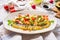 Close up of hummus plate topped with olive oil, avocado, fresh vegetables and herbs served on kitchen table, top view. Vegan food