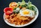 Close up image of Asian pineapple fried rice with fried egg, shrimp, and vegetables salad on a white plate and black background