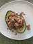 Close up image of avocado halves filled with grey shrimp on a white plate against a green background