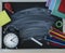 Close up image of blackboard with chalk trace in center of board, colorful school supplie and black clocks in corners of board.