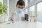 Close up image of boy in  mask, gloves and  white medical coat holding a pipette and glass before examining with a microscope.