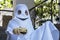 Close up image of boy in white costume of halloween ghost sits on porch of house and holds decorated pumpkin, ready for celebratio