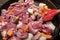 Close up image of meat with vegetables frying in the pan with red kitchen shovel. Above view,