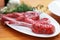 Close up image of Raw beef bone rib-eye steak on a plate with onion, garlic and garnish ready to cook on a wooden table