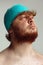 Close-up image of red-headed man in swimming hat posing isolated on gray studio background. Concept of sport, humor and