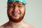 Close-up image of red-headed man in swimming hat posing isolated on gray studio background. Concept of sport, humor and