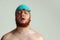 Close-up image of red-headed man in swimming hat posing isolated on gray studio background. Concept of sport, humor and