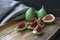 Close up image of ripe green cutted fig lie on wooden cutting board, next to gray textile on wooden tray on dark