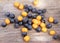 Close-up of image of scattered fresh sea buckthorn berries and chokeberry on wooden surface. Handful of berries gathered.