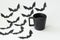 Close up image of Silhouettes of black paper halloween bats and black cup of hot tea on light background.