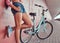 Close-up image of smooth slim female legs in blue sneakers, leaning against a pink wall, near blue city bike
