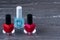 Close-up image of Two Red nail polish bottles and one colorless nail polish bottle on grey wooden background