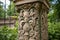 close-up of intricate carvings on stone pillar, with greenery in the background