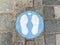 Close up of isolated blue marking sign with feet on the floor to wait here and keep distance while queueing at shop entrance