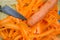 Close up of isolated raw fresh carrot cut in stripes with blade of japanese kitchen knife on wood cutting board