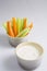 Close up isolated shot of a mixed bowl of crunchy orange carrot slices and juicy green celery sticks with a white cup of blue