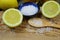 Close up of isolated sliced yellow citrus fruits, blue bowl and wooden spoon with coarse sea salt grains on wood cutting board