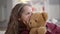 Close-up of joyful pretty child sharing secrets with teddy bear. Beautiful Caucasian cheerful girl whispering on ear of