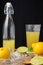 Close-up of juicer with half lemons, mint, bottle with juice and glass, black background, vertical,