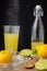 Close-up of juicer with half lemons, mint, bottle with juice and glass with falling sugar, black background,