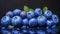 Close-Up Of Juicy Blueberries With Water Droplets And Green Leaves On A Dark Reflective Surface