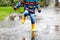 Close-up of kid wearing yellow rain boots and walking during sleet, rain and snow on cold day