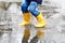 Close-up of kid wearing yellow rain boots and walking during sleet, rain and snow on cold day