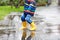 Close-up of kid wearing yellow rain boots and walking during sleet, rain and snow on cold day. Child in colorful fashion