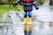 Close-up of kid wearing yellow rain boots and walking during sleet, rain and snow on cold day. Child in colorful fashion