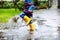 Close-up of kid wearing yellow rain boots and walking during sleet, rain and snow on cold day. Child in colorful fashion