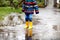 Close-up of kid wearing yellow rain boots and walking during sleet, rain and snow on cold day. Child in colorful fashion