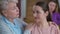 Close-up of kind senior grandmother calming down stressed sad millennial granddaughter as blurred adult mother shouting