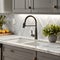 A close-up of a kitchen sink featuring grey cabinets, a white marble countertop, backsplash, and accents