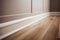 Close up of laminate flooring in a room with white wall and baseboard, strips, molding.