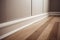Close up of laminate flooring in a room with white wall and baseboard, strips, molding.