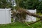 Close up of a large limb that fell off a tree destroying part of a white metal fence leaving a hole.