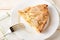 Close-up of large piece of sweet and sour apple pie and fork on a white plate over a white wood table. Easy recipe for sweet