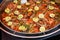 Close up of large portion of cooked fish with red peppers, onion, parsley and fresh yellow lemons in a large pan at a street food