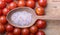 Close-up of a large wooden spoon with coarse pink salt, around delicious small red cherry tomatoes on a natural wooden surface.