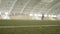 Close-up of lawn in stadium with training athletes. Action. Indoor stadium with green grass and players practicing in