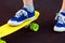 Close up legs in blue sneakers riding on yellow skateboard in motion. Active urban lifestyle of youth, training, hobby, activity