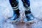 Close up legs of child in rubber boots jumpingin puddles after rain