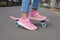 Close-up legs of girl skateboarder in blue jeans and pink sneakers, riding pink penny skate longboard.