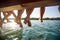 Close-up of legs of a group of friends sitting on the dock on the river. Summer, river, vacation