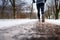 Close-up at legs of a male runner jogging in a park cover by snow.